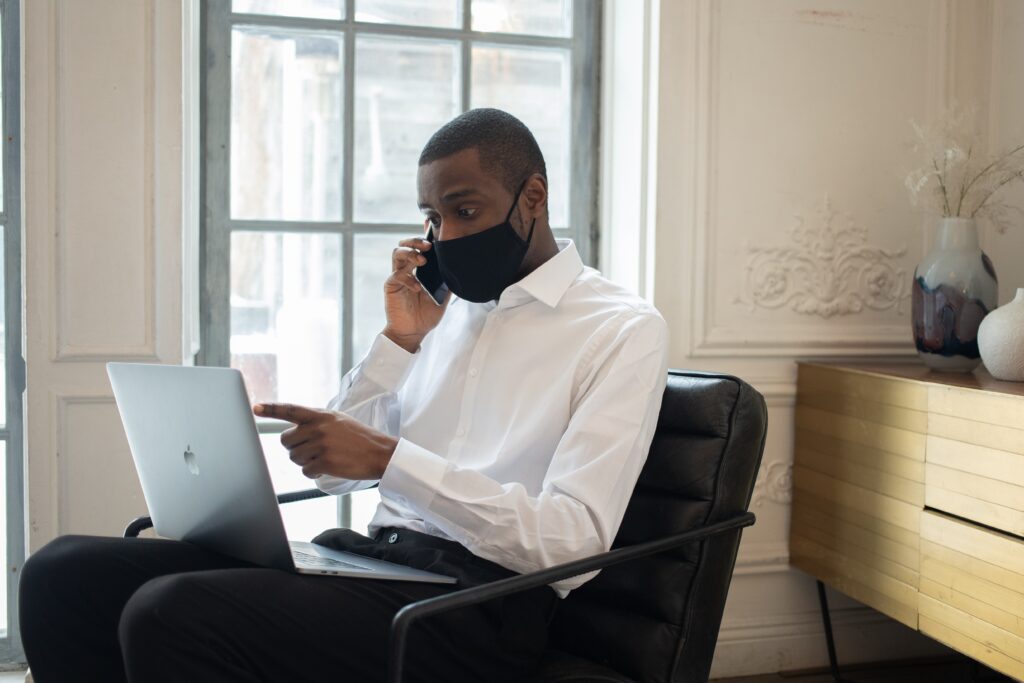 A man sitting in front of a laptop on his phone.