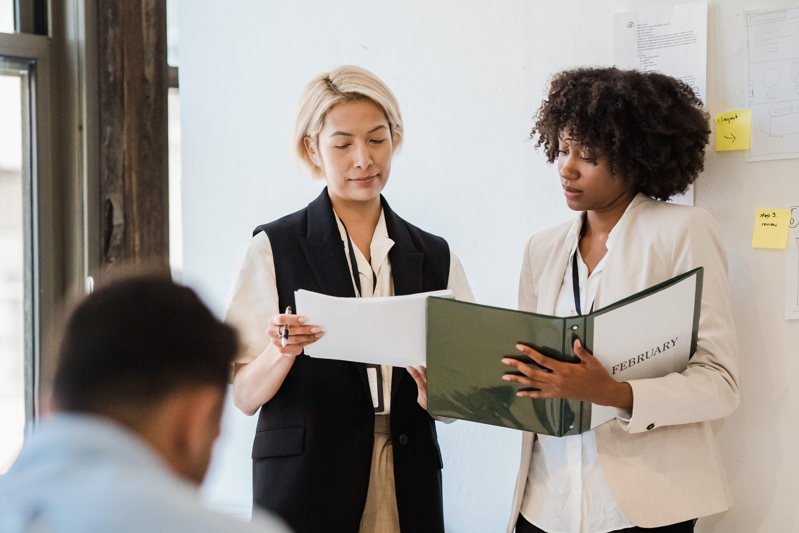 Two women are standing in a room with papers.